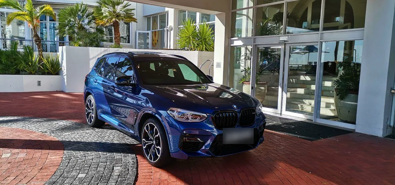 A blue BMW X3 M parked at a hotel entrance