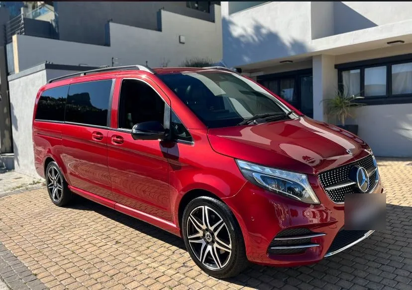 A red Mercedes-Benz V-Class parked outside a modern house